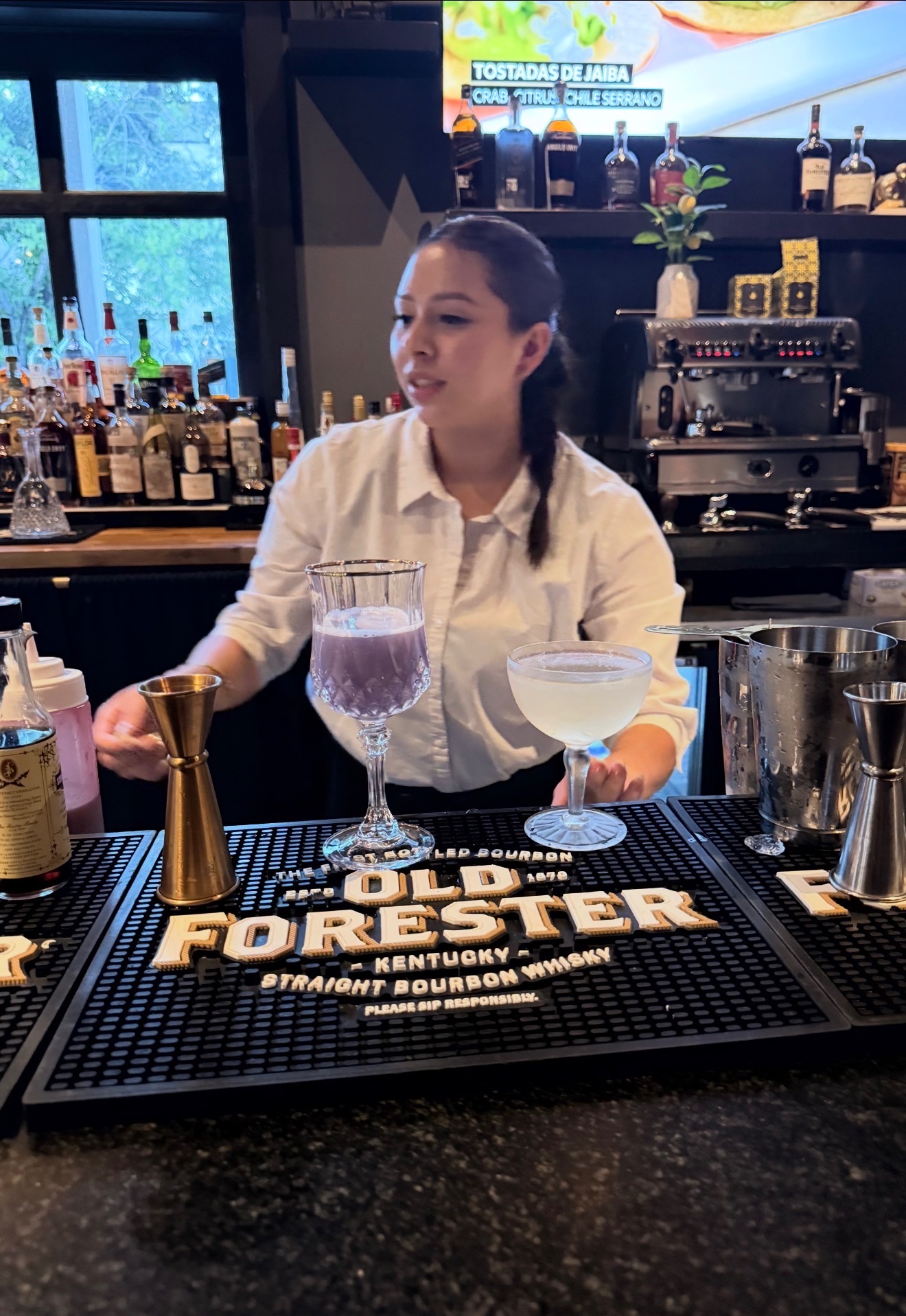 A bartender at the bar with two finished cocktails