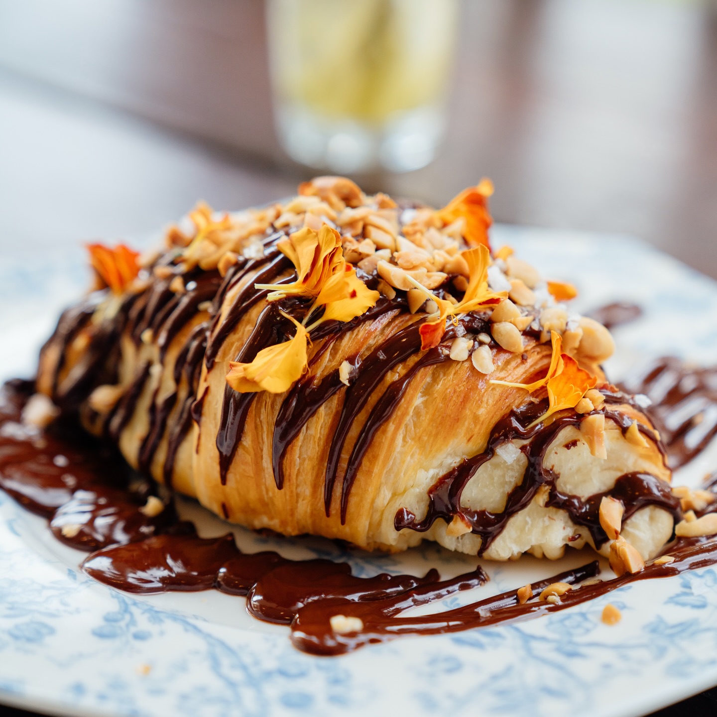 A croissant filled with cream, drizzled with chocolate and scattered with nuts