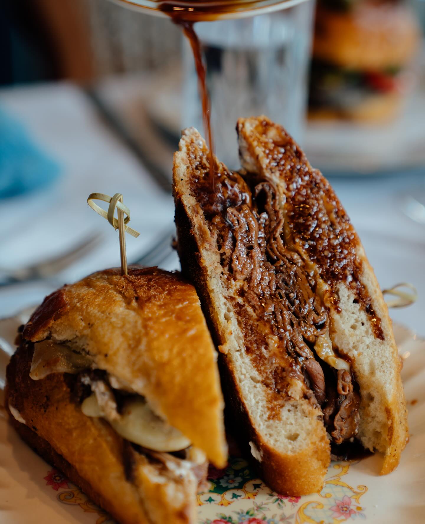 A French dip sandwich cut in half with jus being poured over it