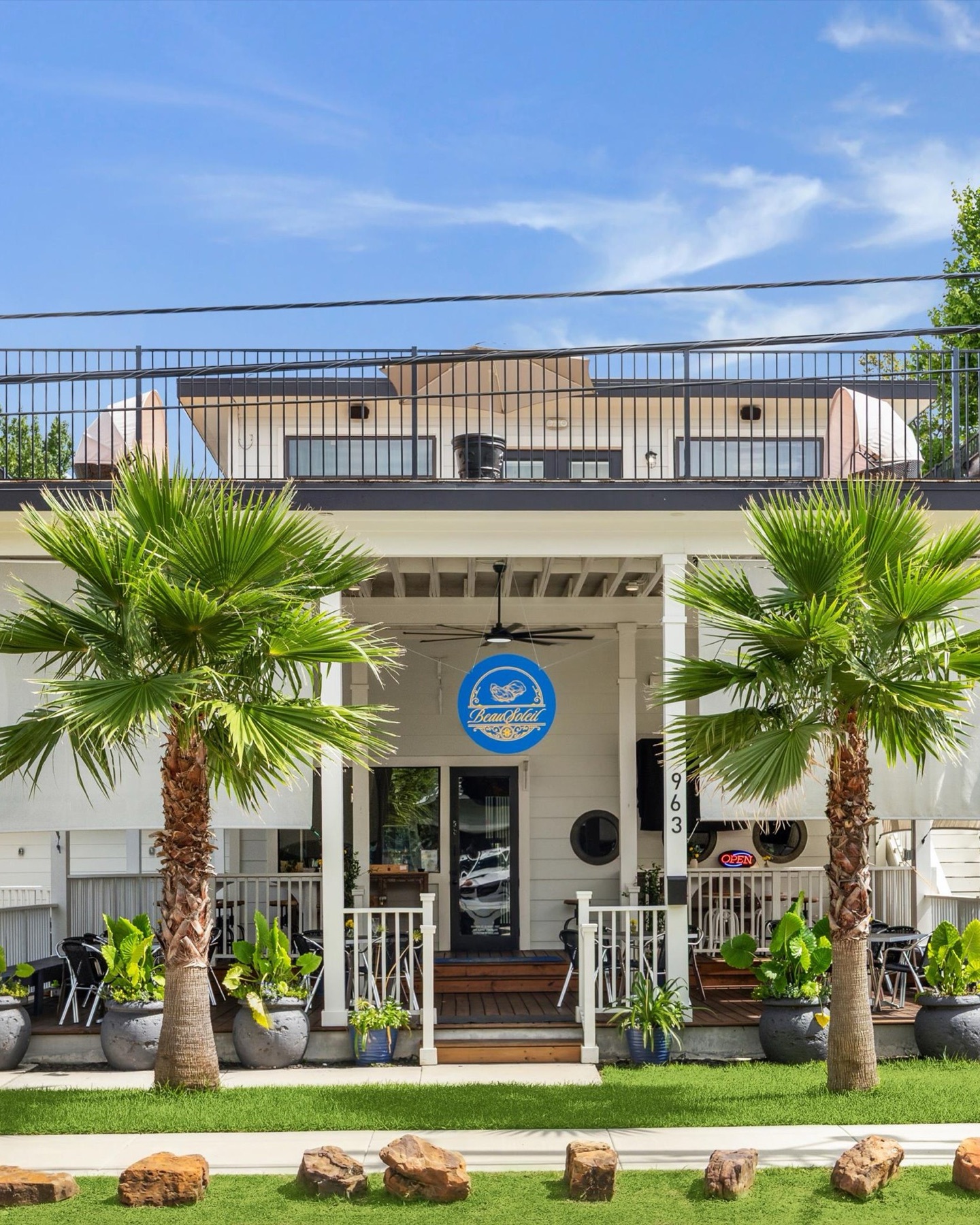 The restaurant seen from the street, a white two storey building with a palm either side of the porch and the blue Beausoleil sign above the door