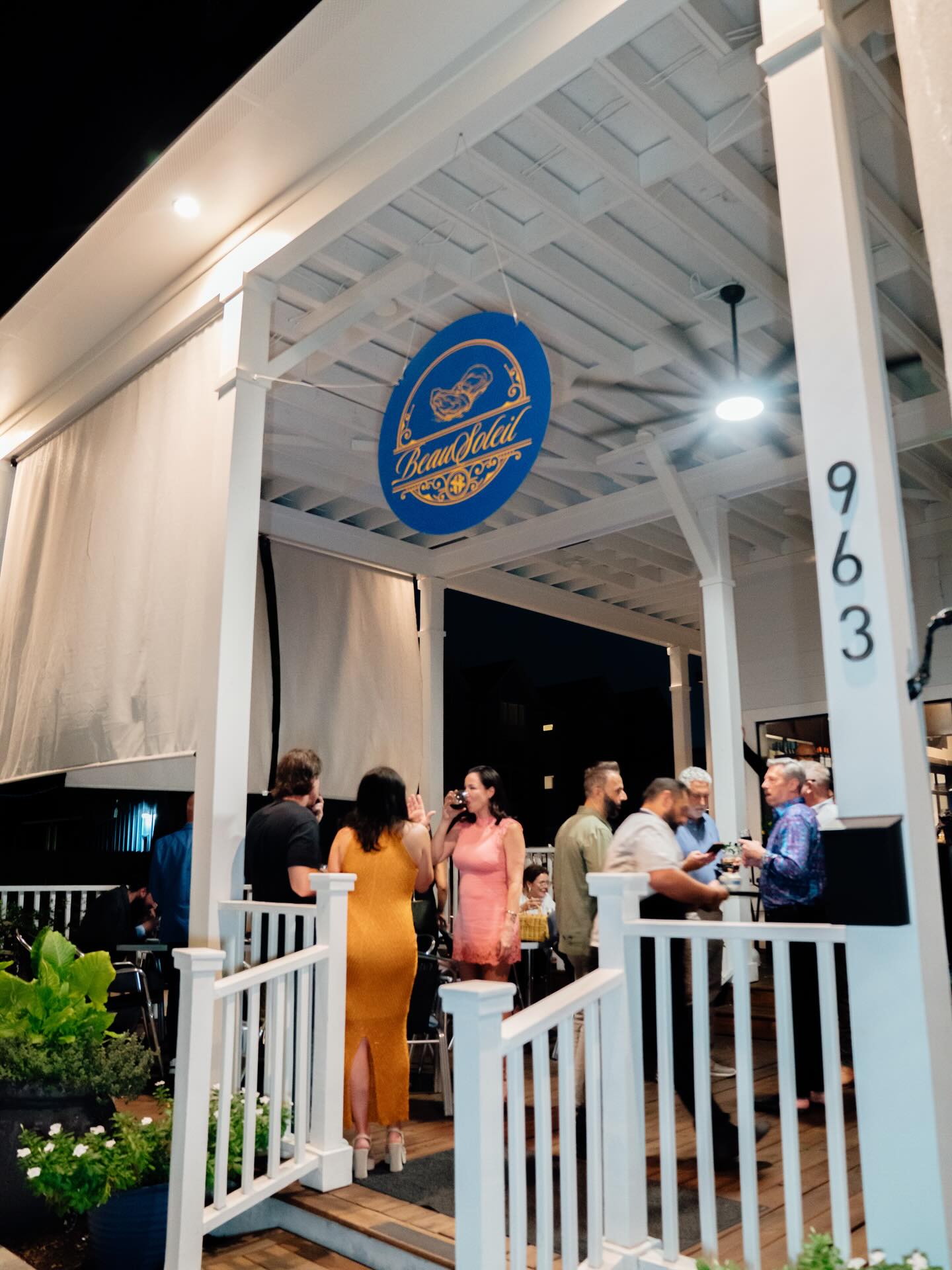 Guests on the front porch at night under the lit Beausoleil sign