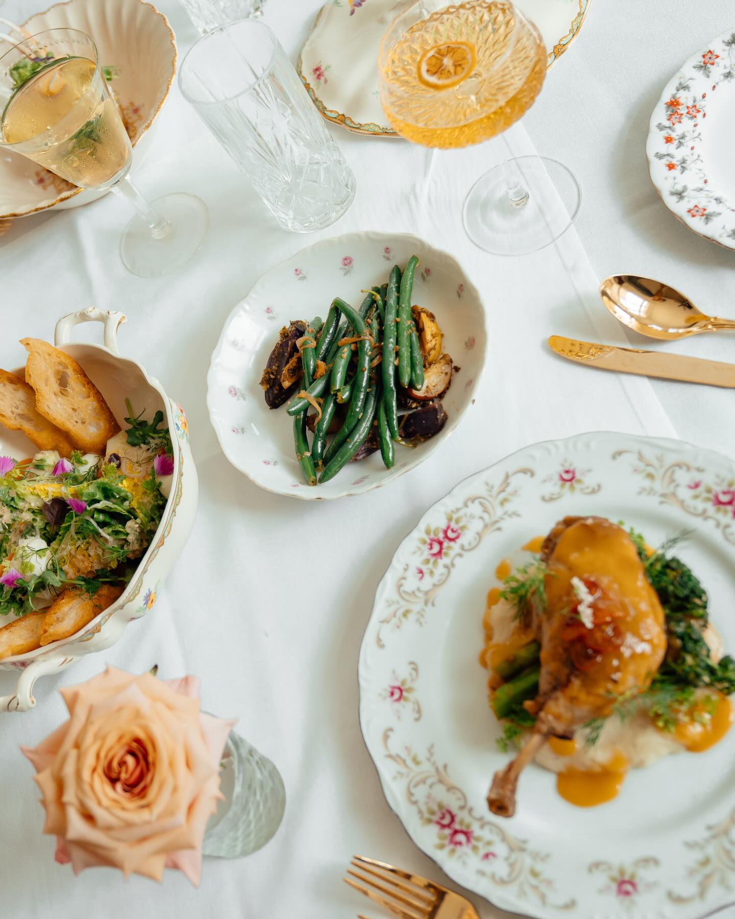 A long table laid for a party with plates, roses and gold cutlery
